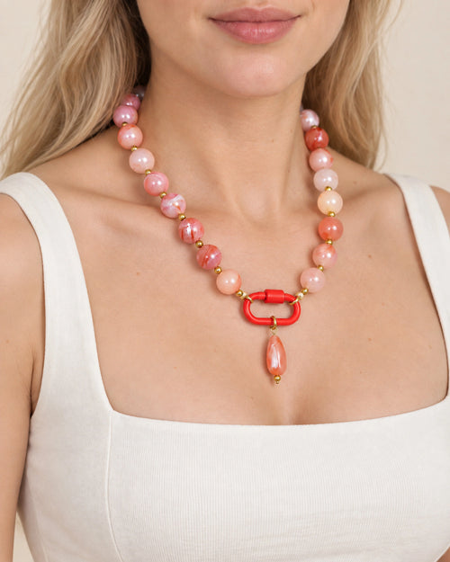 Coral pink and white acrylic beaded necklace with a pink oval pendant, worn at the neckline.