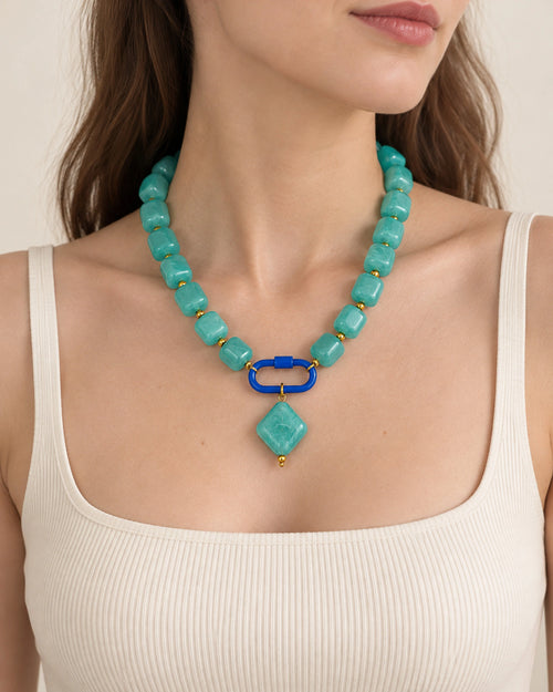 Turquoise blue acrylic beaded necklace with a turquoise-colored diamond pendant, worn at the neckline.
