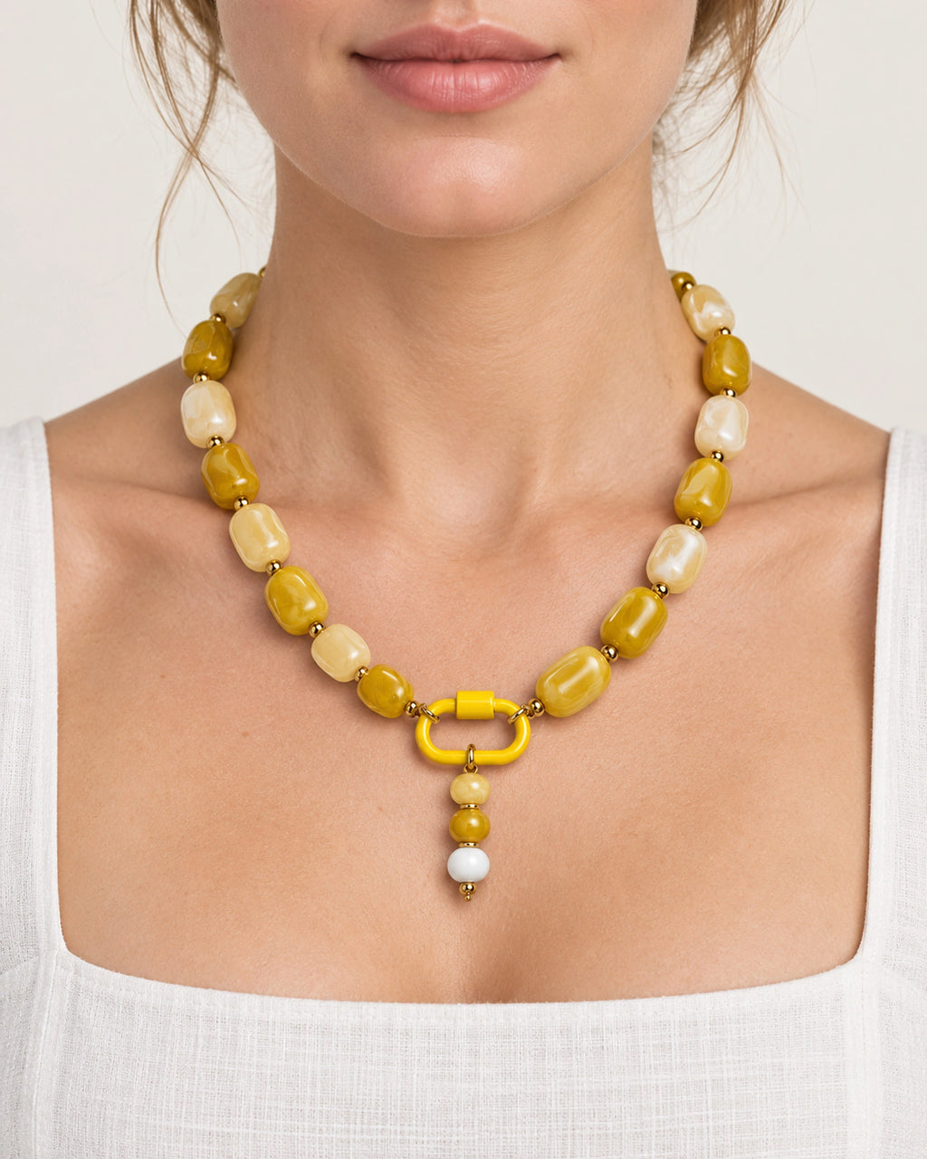 Yellow and cream acrylic beaded necklace with a yellow and white beaded drop pendant, worn at the neckline.