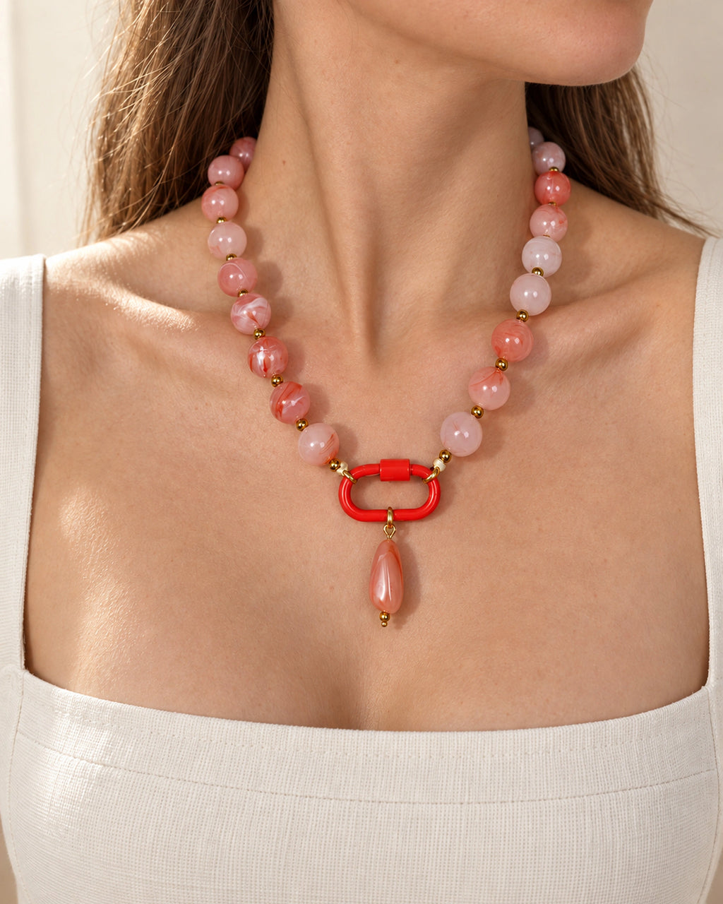 Coral pink and white acrylic beaded necklace with a pink oval pendant, shown in a close-up styling view.