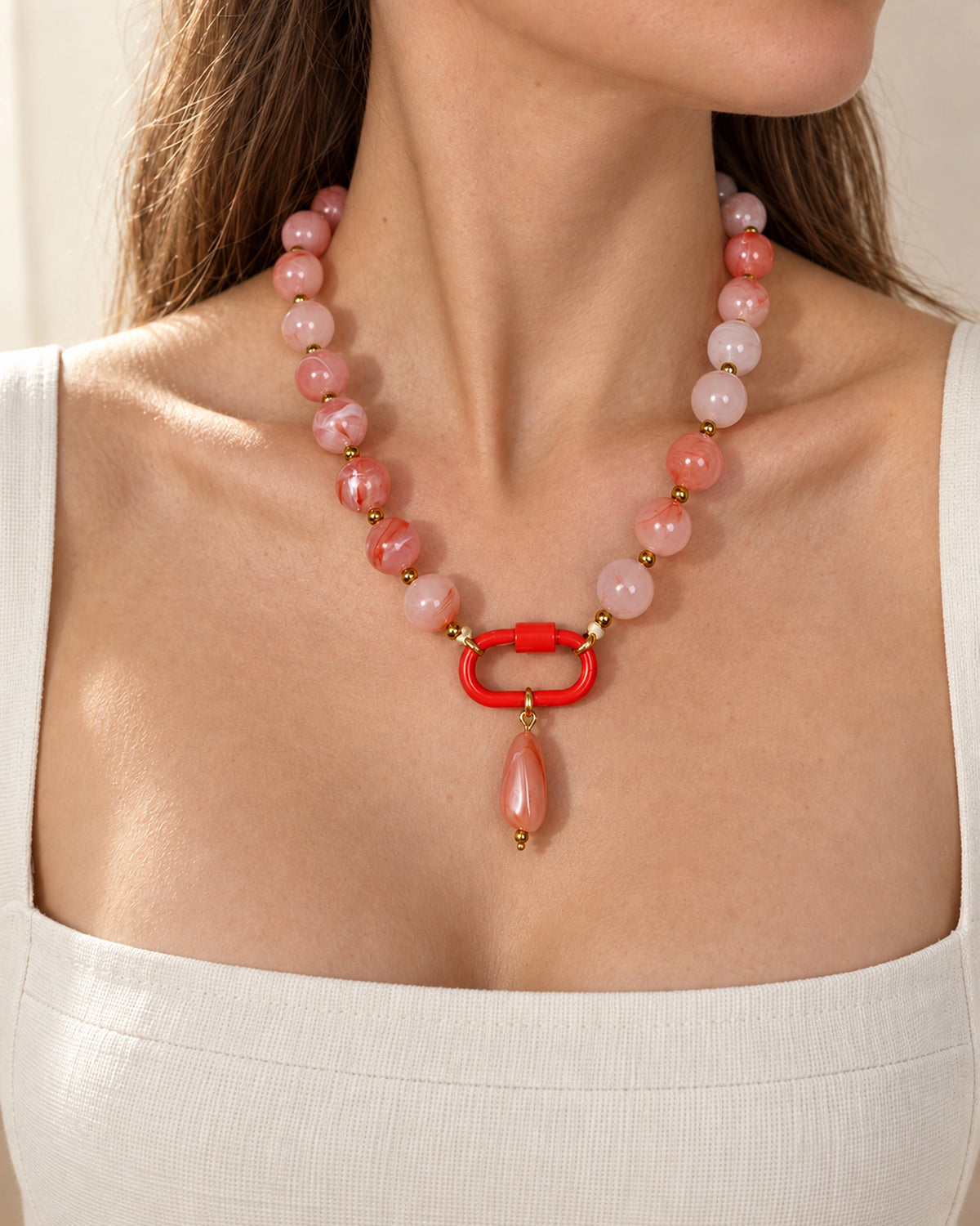 Coral pink and white acrylic beaded necklace with a pink oval pendant, shown in a close-up styling view.