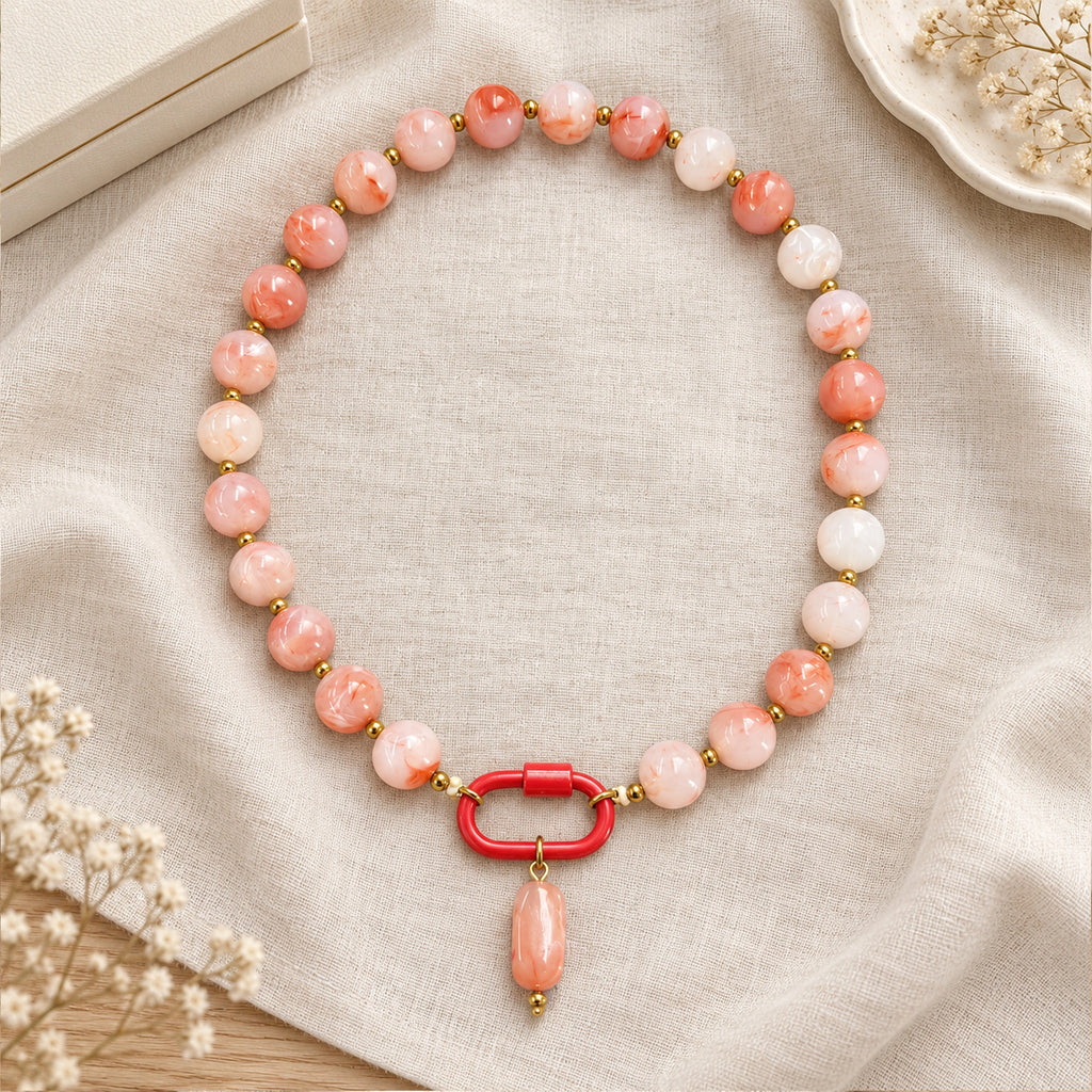 Coral pink and white acrylic beaded necklace with a pink oval pendant arranged in a styled still-life setting.