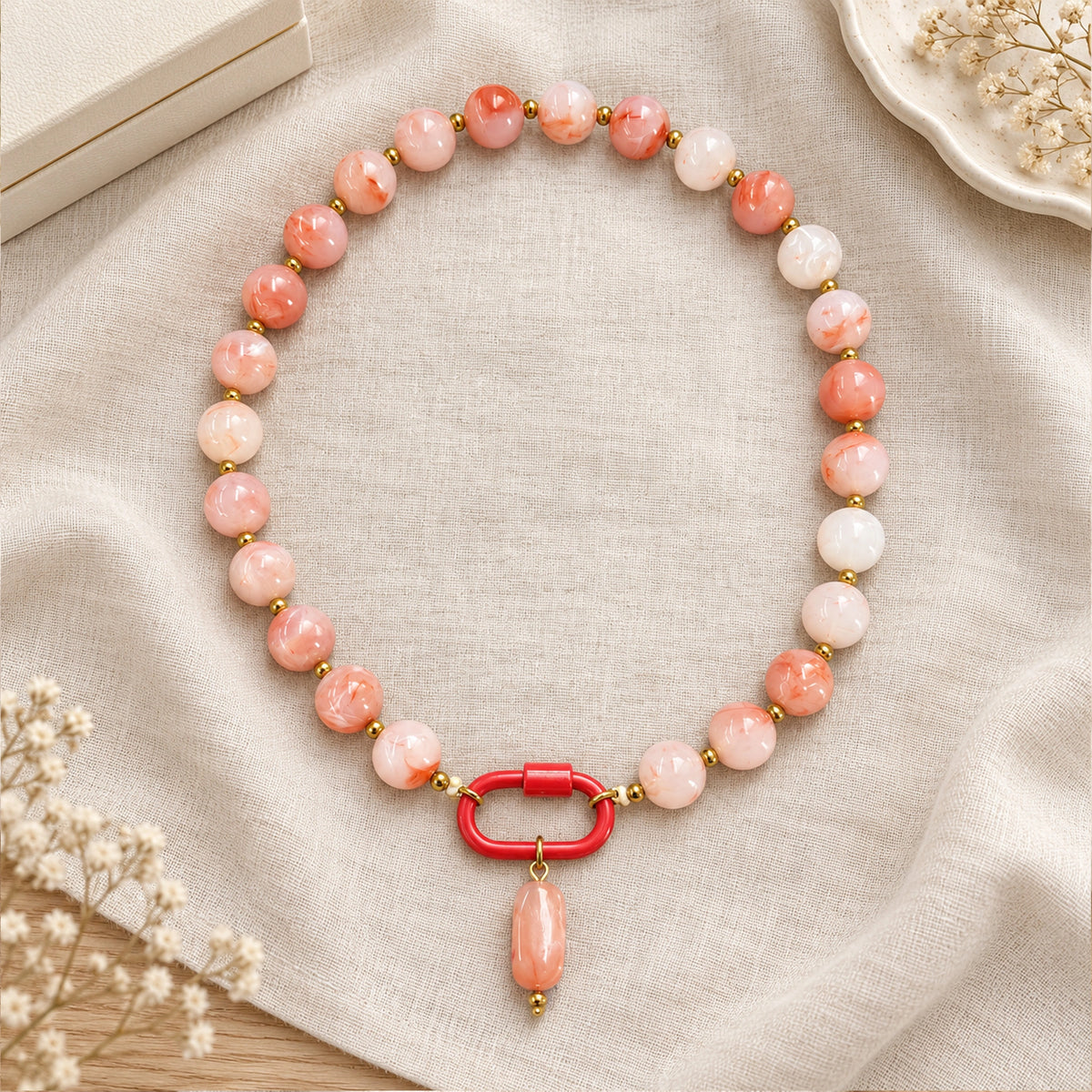 Coral pink and white acrylic beaded necklace with a pink oval pendant arranged in a styled still-life setting.