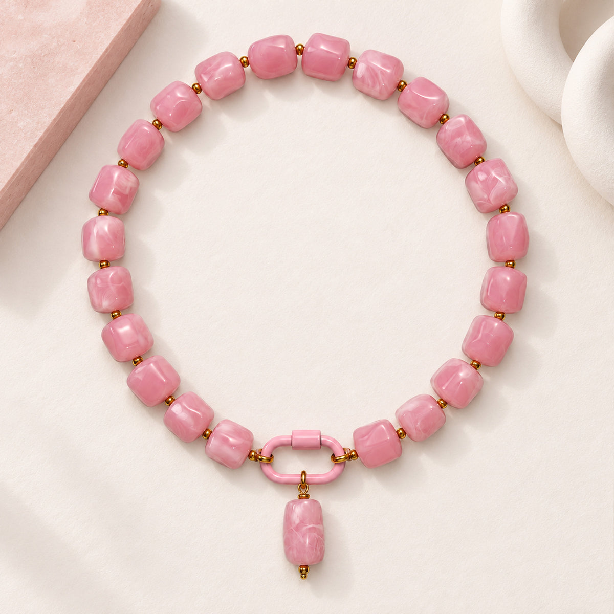 Pink acrylic beaded necklace with a pink oval pendant arranged in a styled still-life setting.