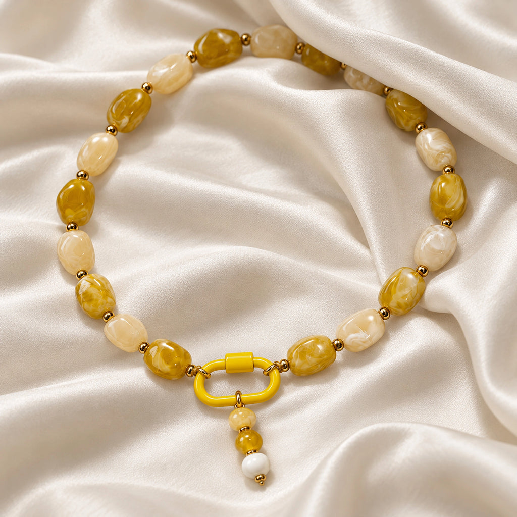 Yellow and cream acrylic beaded necklace with a yellow and white beaded drop pendant arranged in a styled still-life setting.