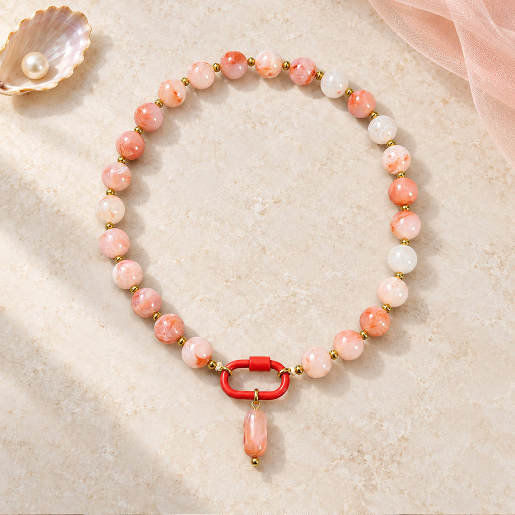 Coral pink and white acrylic beaded necklace with a pink oval pendant arranged in a styled still-life setting.