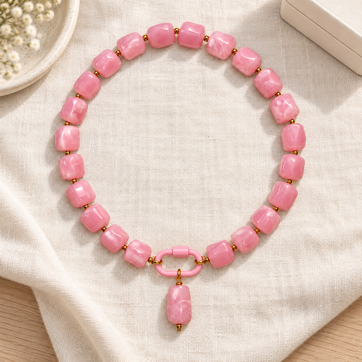 Pink acrylic beaded necklace with a pink oval pendant arranged in a styled still-life setting.