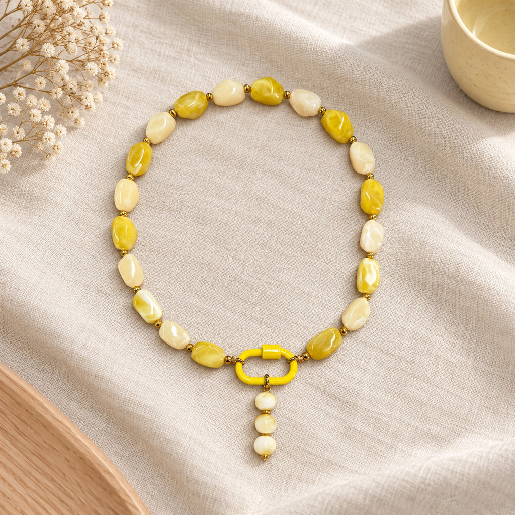 Yellow and cream acrylic beaded necklace with a yellow and white beaded drop pendant arranged in a styled still-life setting.
